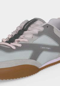 Sneaker Calvin Klein σε γκρι και ανοιχτό ροζ με υφασμάτινα κορδόνια και σόλα από καουτσούκ, με εμφανές το όνομα της μάρκας στο πλάι και στη γλώσσα.