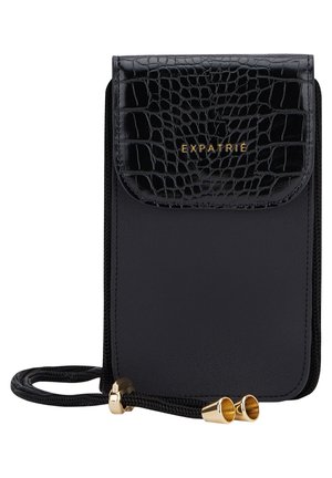 Musta nahkainen crossbody-laukku krokotiilikuviollisella läpällä, kultaisella "EXPATRIE"-tekstillä ja säädettävällä naruhihnalla, jossa kultaiset metalliset päät.