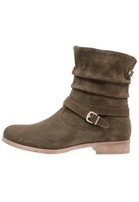 Bottine en daim vert kaki avec une tige froncée, un panneau à texture tissée et une lanière latérale ornée d'une boucle argentée. Semelle plate en bois.