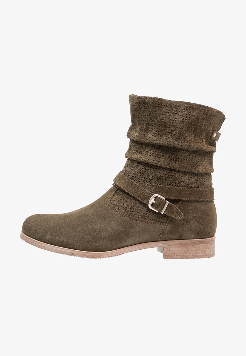 Bottine en daim vert kaki avec une tige froncée, un panneau à texture tissée et une lanière latérale ornée d'une boucle argentée. Semelle plate en bois.