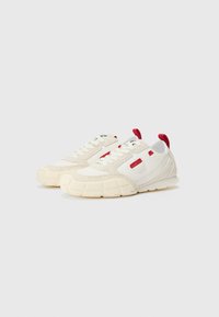 Baskets blanches avec des accents beige texturé, des onglets rouges et un design contrasté. Comprend une semelle épaisse et patternée et un système de laçage.