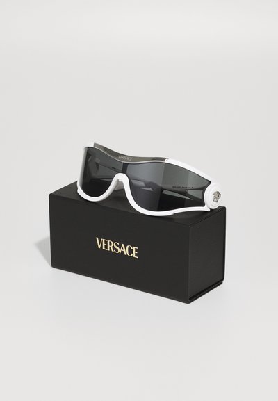 Versace sunglasses feature a wide frame in white with dark lenses, housed in a black box with gold lettering. Notable logo detail on the arm.