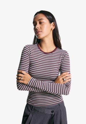 Long-sleeve top in maroon with white and light blue horizontal stripes. Features a crew neckline and fitted design. Worn with dark grey trousers.