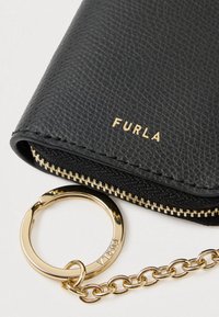Borsetă din piele texturată neagră cu fermoar și accesorii aurii, având un inel auriu pentru chei atașat. Numele mărcii „Furla” este embosat în aur.