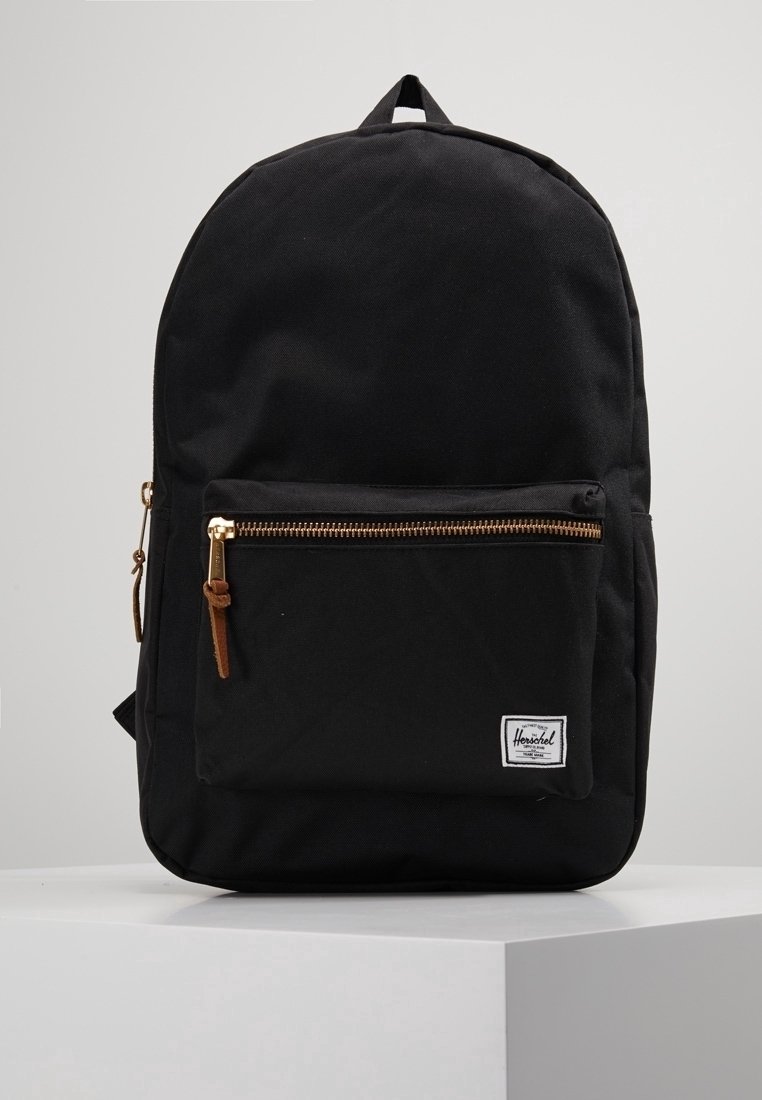 Sac à dos Herschel noir avec poche zippée à l'avant, curseurs de fermeture en cuir et étiquette de marque blanche sur une surface blanche propre.