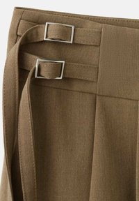 Tissu marron à finition texturée, présentant deux accents en métal argenté carrés et un détail de ceinture nouée à la taille.