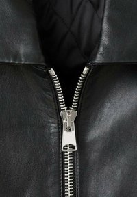 Zwarte leren jas met een kraag en een zilveren ritsdetail. De binnenkant heeft een gewatteerde zwarte voering, wat een soepele textuur benadrukt.