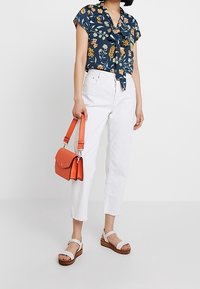 Blusa azul marino con estampado floral, de mangas cortas y un nudo en la cintura, combinada con jeans blancos cortos y un pequeño bolso naranja.