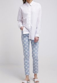 Vit långärmad skjorta med knappar, ljusblå prickiga jeans och vita slip-on sandaler. Avslappnad outfit med en ledig passform och klassisk design.