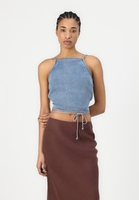 Denimski crop top s podesivom vezicom na rubu, u svijetloplavoj boji s tankim naramenicama, u kombinaciji s smešnim suknjom.