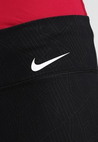 Leggings sportivi neri con un design testurizzato, dotati di un logo Nike bianco. La parte superiore è rossa, evidenziando la cucitura tra i colori.