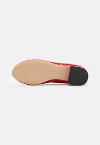 Red flat shoe showing smooth beige sole with black heel grip and faint "Steve Madden" branding.