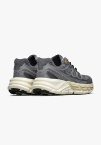 Scarpe sportive grigie realizzate con una combinazione di suede e materiali in mesh, suola bianca spessa, dettagli texturizzati e occhielli gialli per i lacci.