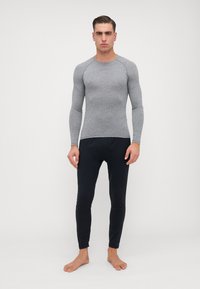 Šedá dlouhá termo trička s fitted designem a kulatým výstřihem. V páru s černými fitted legínami, obojí vyrobené z hladkého materiálu.
