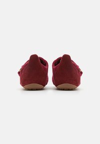 Burgundske suede cipele s zaobljenim stražnjim dijelom, teksturiranom površinom i fleksibilnom gumenom zakočkom. Imaju mali zlatni detalj blizu pete.