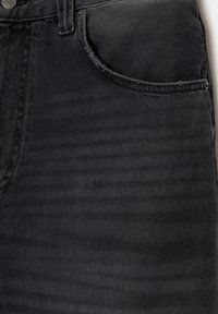 Gros plan d'un jean en denim noir montrant la poche avant, la boucle de ceinture et les détails visibles des coutures.