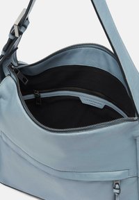 Borsa in pelle azzurro chiaro con apertura a zip, fodera in tessuto nero, tasca interna e tracolla regolabile. Accenti hardware minimi visibili.