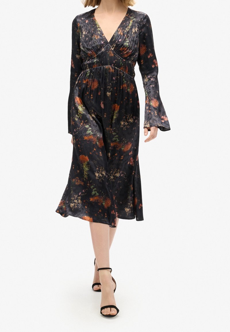 Robe noire à motifs floraux avec manches longues évasées, un décolleté en V profond et une taille cintrée, présentant des motifs floraux colorés sur toute la surface.