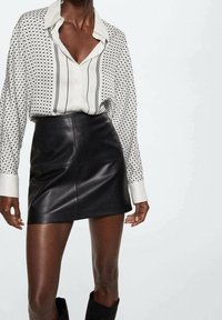 Long-sleeve button-up shirt in white with black polka dots and stripes, paired with a high-waisted black leather mini skirt.