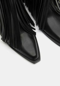 Črne usnjene gležnjarje z dolgimi, ravnimi frufrkami, koničastimi prsti in gladko teksturo z mat površino.