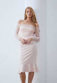 Robe décolletée en rose clair avec des manches longues en dentelle, corsage ajusté et ourlet évasé. Tissu lisse avec un subtil éclat.