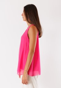 Top senza maniche di colore rosa, realizzato in tessuto leggero, con una vestibilità ampia e un orlo arrotondato, caratterizzato da una texture liscia e un design minimale.