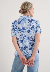 Short-sleeved shirt in light blue with a floral pattern in dark blue and light blue shades. Material appears lightweight; featured in a relaxed fit.