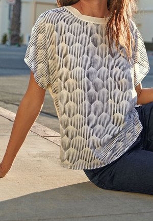 Top de manga corta en blanco y azul marino con un patrón texturizado de olas. Presenta un cuello redondo y un corte holgado.