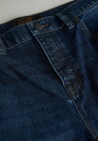 Granatowe dżinsy z denimu o prostych nogawkach, zapinane na guziki, z subtelnymi przeszyciami wzdłuż talii i kieszeni.