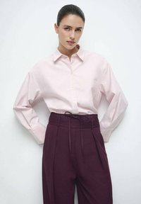 Lichtroze overhemd met knopen, lange mouwen en een borstzak, gecombineerd met hoog getailleerde, diep bordeauxrode broek met een aansluitende tailleband.