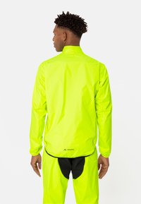 Veste imperméable jaune fluo avec un col haut, des manches longues et un logo au dos. Matériau lisse et léger avec une coupe ample.