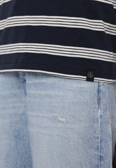 Marinblå og hvide stribede bomulds t-shirt med rund kant, parret med lyseblå slidte denim jeans med en sidelabel detalje.