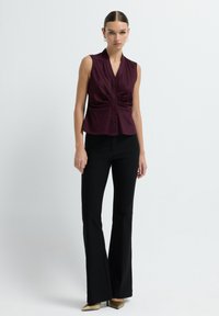 Blouse sans manches bordeaux avec un décolleté en V, fermeture à boutons sur le devant et détails froncés. Associée à un pantalon noir évasé et des escarpins dorés à bouts pointus.