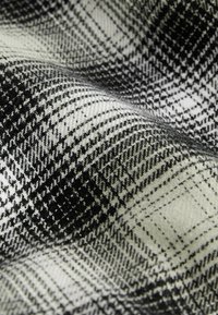 Tissu pied-de-poule noir et blanc avec un motif tissé texturé et des plis doux créant des ombres et de la profondeur.