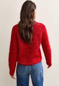 Czerwony miękki sweter z fakturowanym wykończeniem, długimi rękawami i luźnym krojem, zestawiony z niebieskimi jeansami z wysokim stanem.