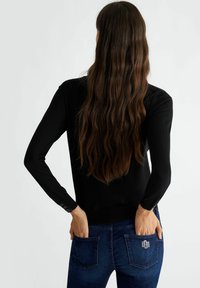 Maglione nero a maniche lunghe con dettagli a bottoni sui polsini, abbinato a jeans in denim scuro con dettagli in strass sulle tasche posteriori.