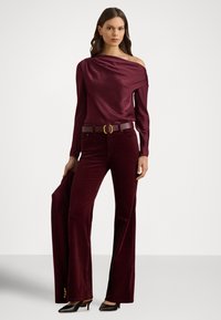 Vínový saténový top s odhalenými ramenami v kombinácii s zamatovými zvonovými nohavicami, doplnený opaskom s kruhovou prackou a jemnými gombíkmi na leme.