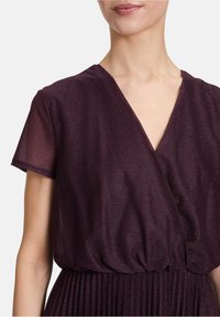 Robe portefeuille prune avec un décolleté en V profond, des manches courtes et une texture légèrement pailletée, dotée d'une taille froncée et d'une jupe plissée.