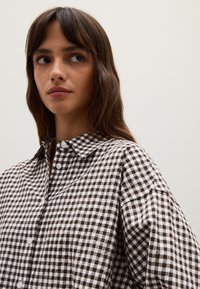 Bruine en witte geblokte shirt met een kraag, knoopdetails en een losse pasvorm, gemaakt van een lichtgewicht stof.