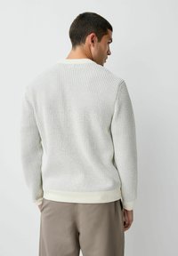Pulover din lână de culoare crem deschis, cu un model texturat, guler, manșete și tiv ribbate. Țesătura are un țesut liber pentru o bună ventilație. Vedere din spate elegantă.