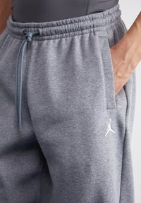 Szare spodnie dresowe wykonane z miękkiego materiału, z elastyczną talią, sznurkiem i bocznymi kieszeniami oraz białym logo przy krawędzi.