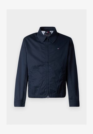 Tengerészkék dzseki galléros nyakkal, elülső cipzárral és oldalsó zsebekkel. A mellkason egy apró logó található, sima tapintású.