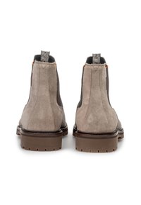 Par de botas Chelsea de ante beige con suelas de goma gruesas marrones, paneles laterales elásticos negros y tiradores estampados en la parte trasera.