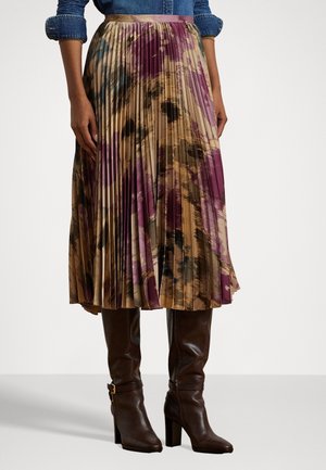 Jupe plissée mi-longue avec imprimé abstrait violet, beige et marron, associée à des bottes hautes marron foncé à talons et une chemise en jean retroussée.