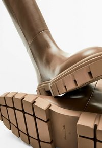 Bruine leren kniehoogte laarzen met een robuuste rubberen zool met een getextureerd patroon. Gladde bovenkant met minimale stiksels en een ronde neus.