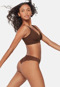 Soutien-gorge wireless marrone e perizoma in pizzo abbinato, caratterizzati da una texture liscia e un design minimalista, con dettagli in pizzo intricati sul perizoma.