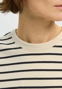 Béžová pruhovaná mikina s černými vodorovnými pruhy, žebrovaným kulatým výstřihem a jemnou, hladkou texturou materiálu. Detail oblasti kolem krku.