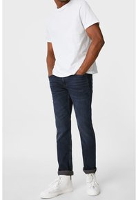 Tmavě modré džíny s úzkým střihem a ohrnutými nohavicemi. Kombinovány s jednoduchým bílým tričkem a bílými teniskami pro ležérní vzhled.