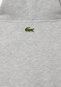 Szara bluza z kapturem wykonana z miękkiego materiału, z małym zielono-czerwonym logo krokodyla na piersi. Prosty design, casualowy styl, bez wzorów.