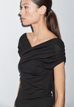 Top nero senza spalle con dettagli drappeggiati e maniche corte. Realizzato in tessuto a coste, presenta una silhouette aderente.